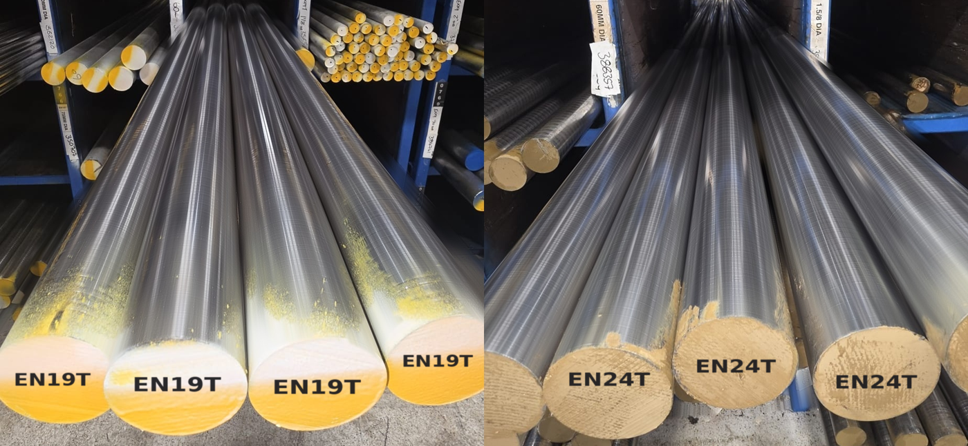 EN19T and EN24T bright round bar in racking at Parkside Steel, photographed along the length so the bars converge into the rack, with the painted bar ends labelled EN19T on the left and EN24T on the right