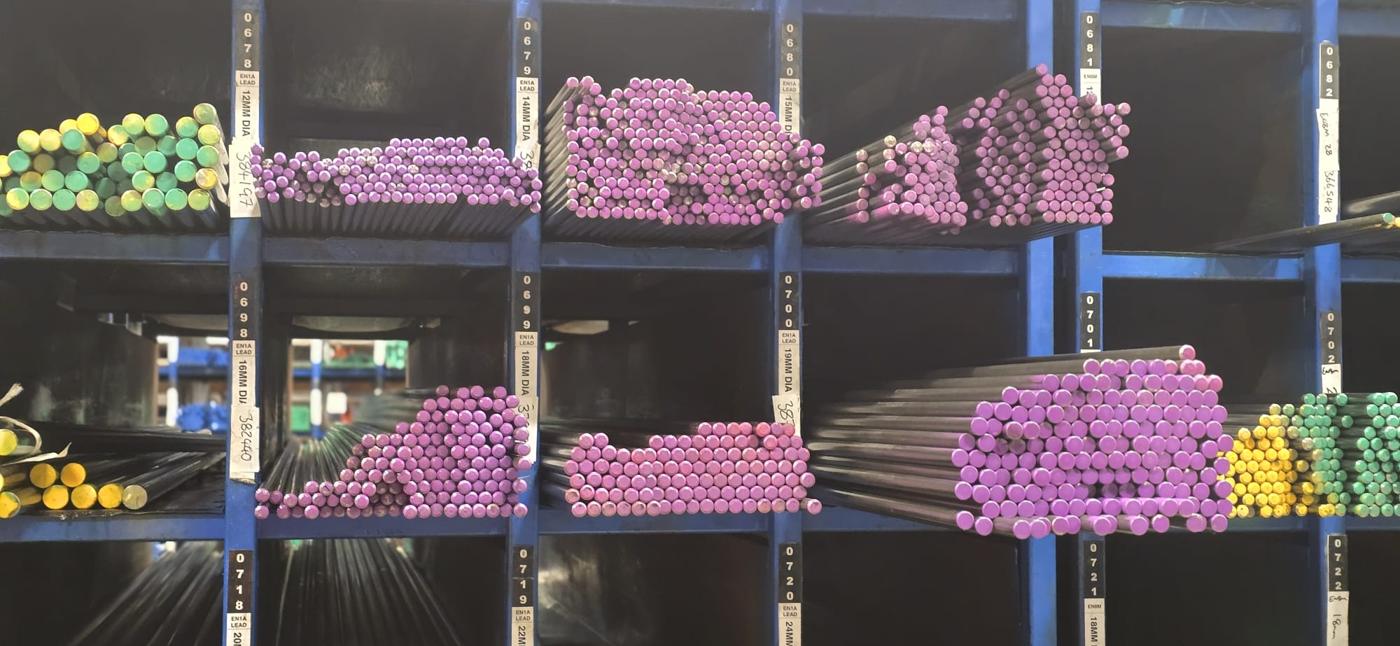 EN1A Pb leaded free-cutting bright round bar in pigeon-hole racking at Parkside Steel, ends paint-marked pink, each location labelled EN1A LEAD with diameter and cast number