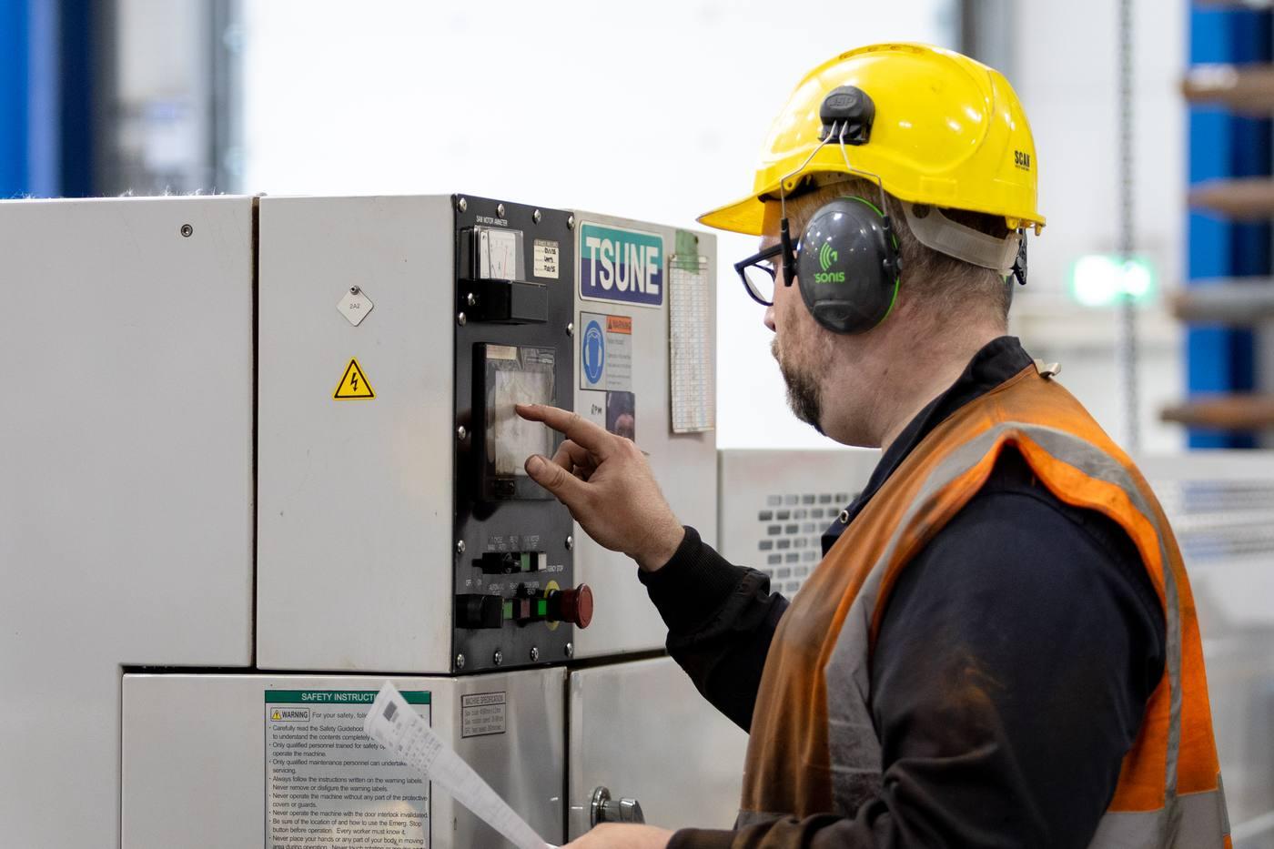 Operative at TSUNE high-speed circular saw control panel — yellow helmet and ear defenders