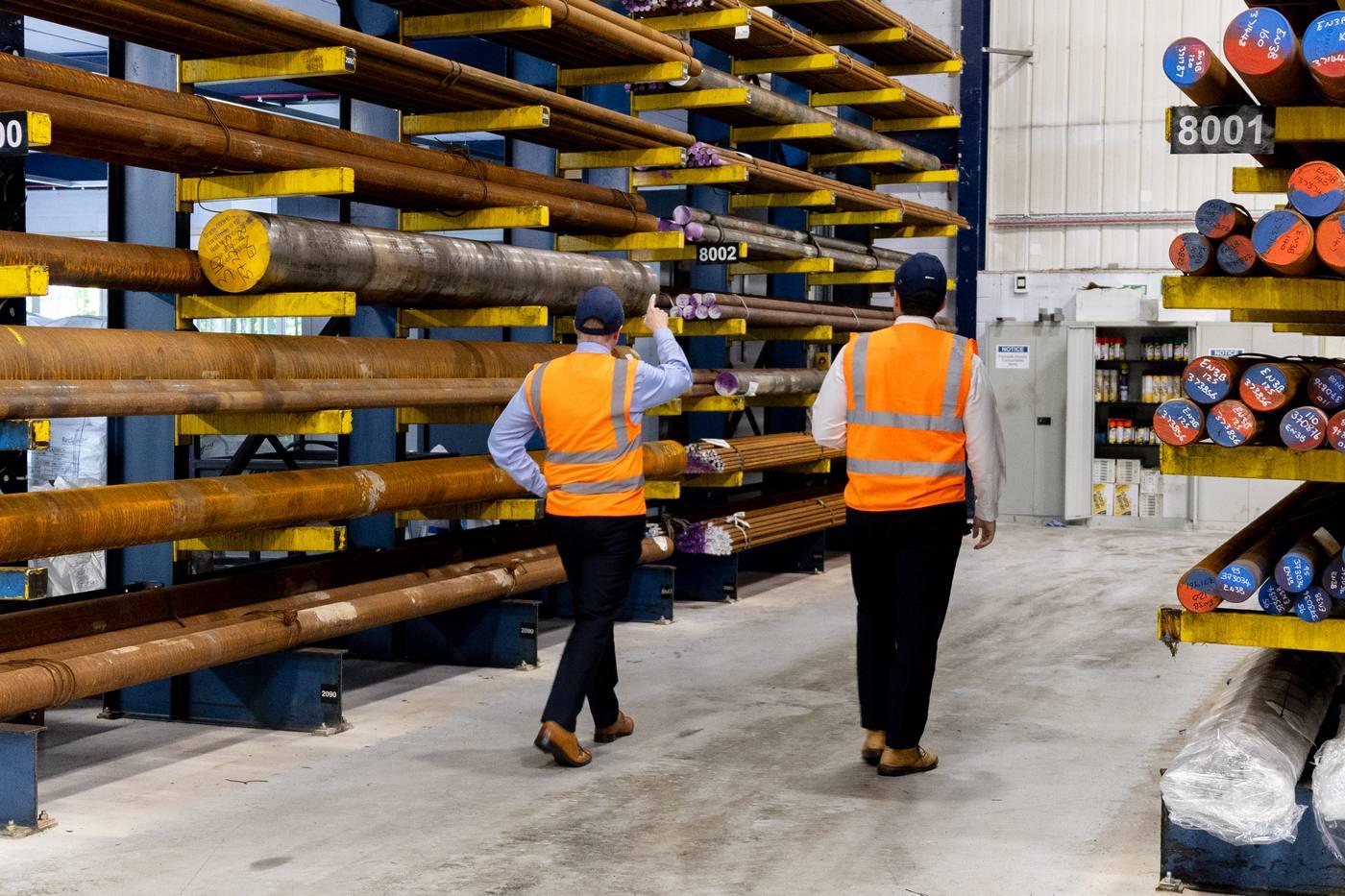 Two Parkside Steel team members walking through large black bar racking — quality stock management