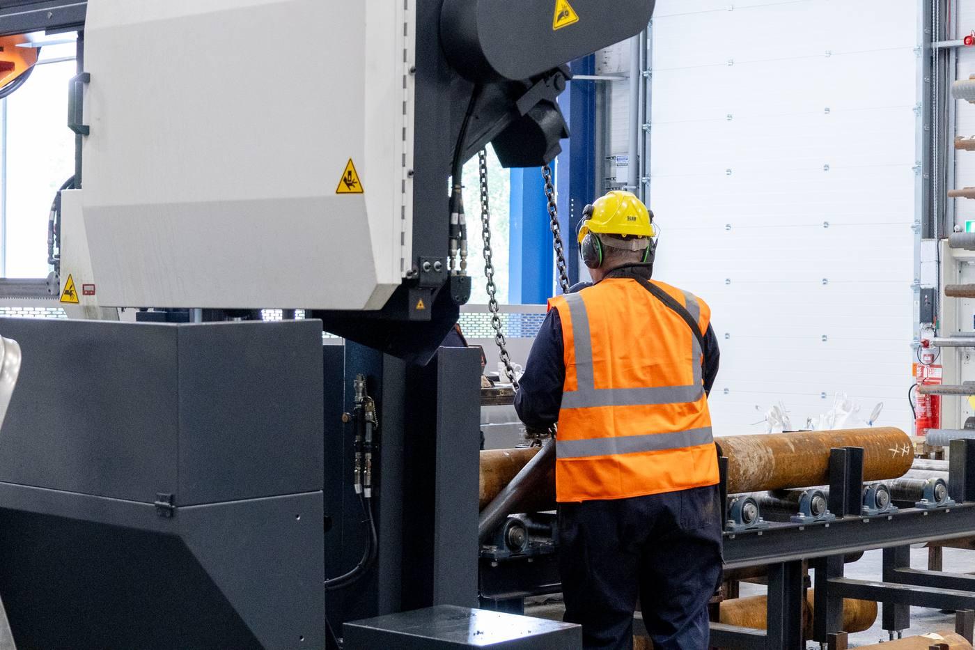 Three operatives loading large diameter black bar into RONTGEN band saw