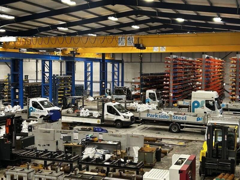 Parkside Steel branded delivery fleet being loaded inside warehouse — saws, racking and overhead crane visible