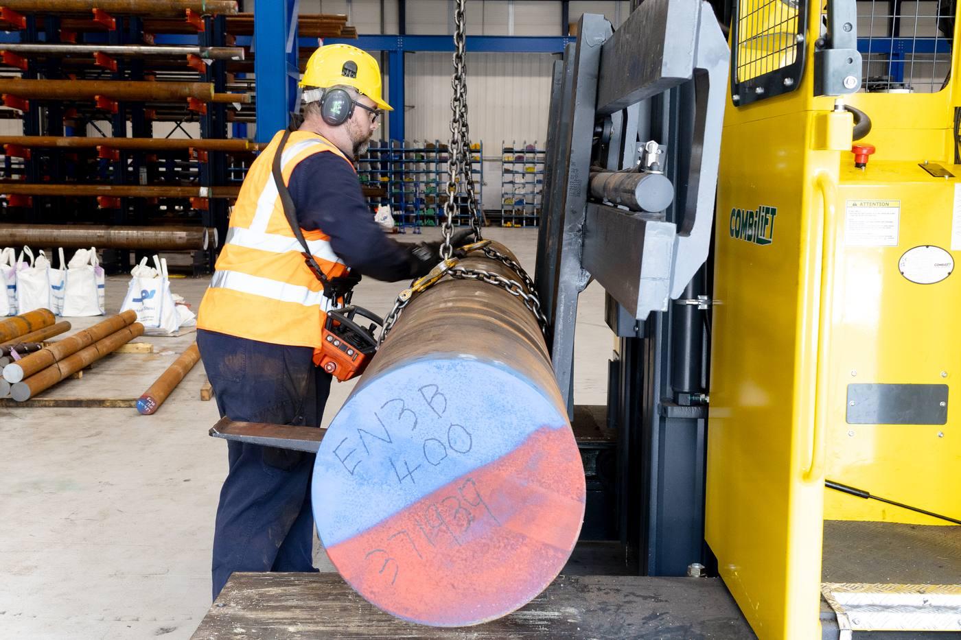 Operative in full PPE loading 400mm EN3B black round bar onto Combilift using chain remote