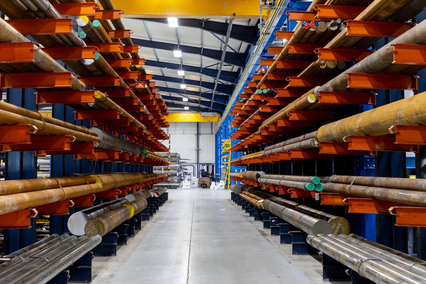 Symmetrical aisle between two walls of orange cantilever racking loaded with large diameter black round bar