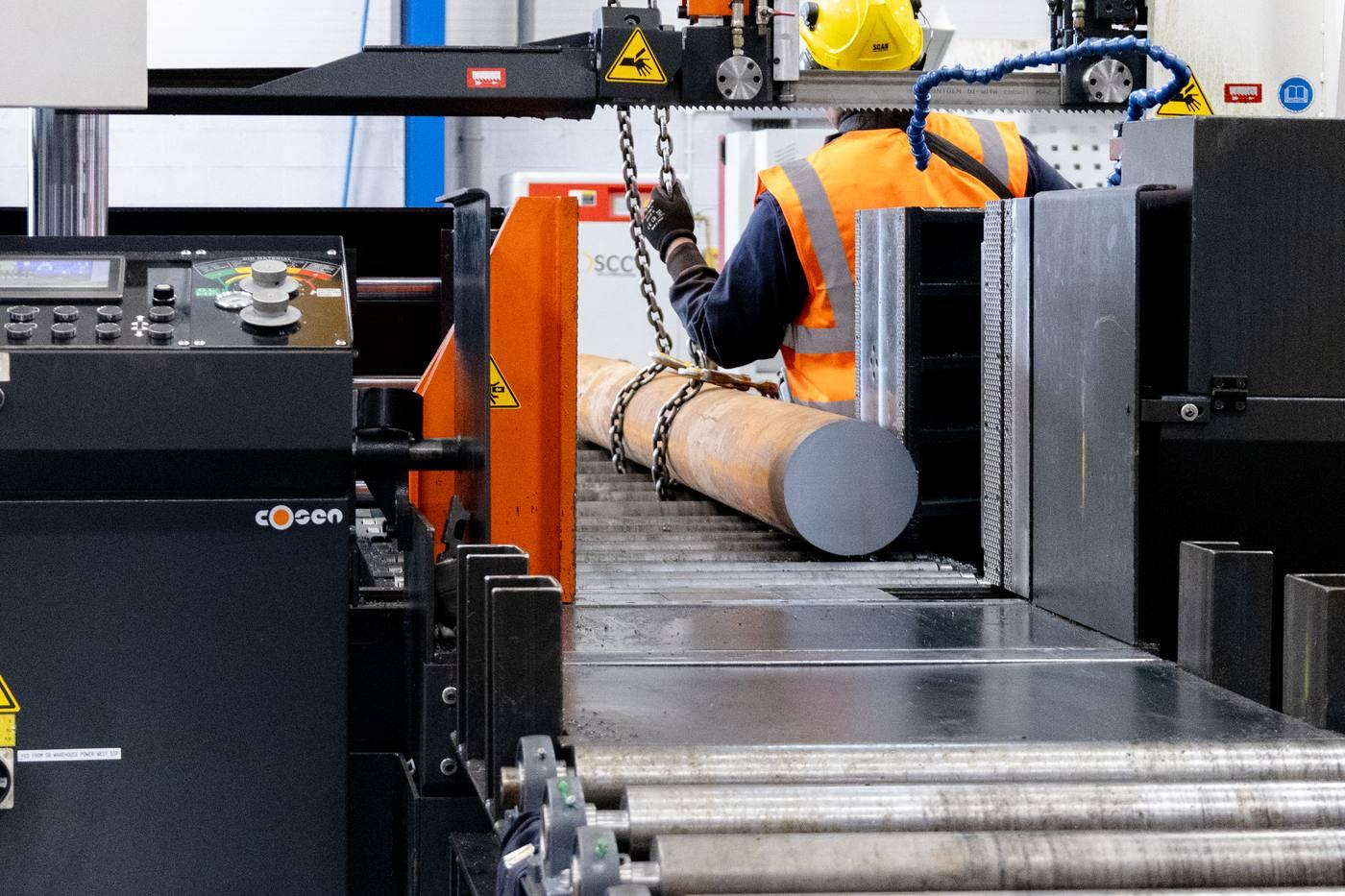 Operative loading large diameter black round bar into COSEN band saw with chain hoist — cut-to-length service