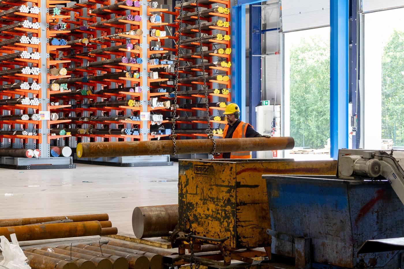 Full-height orange cantilever racking wall with colour-coded engineering steel bar — operative with large bar on chain hoist, open loading bay doors