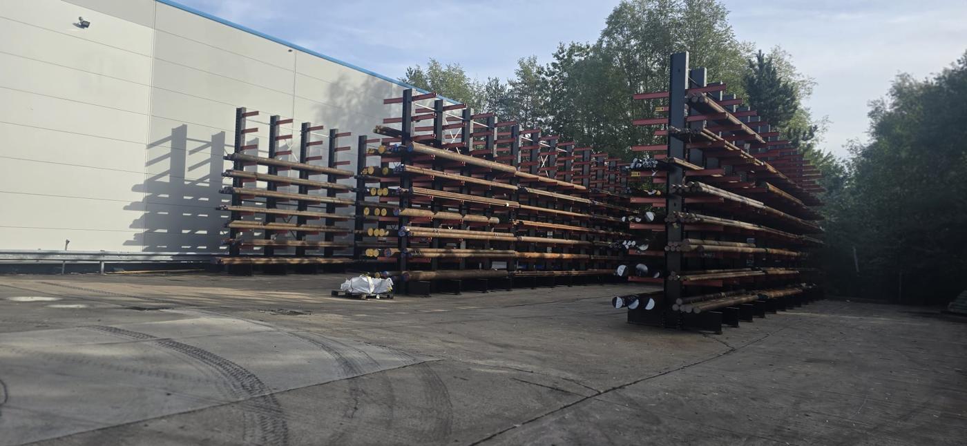 External cantilever racking on the yard at Byron House, loaded with black round bar with paint-marked ends, alongside the warehouse