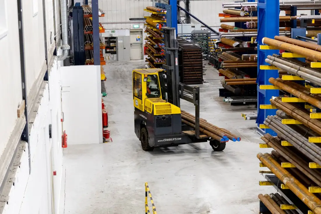 Aerial view from mezzanine — Combilift carrying large black round bar through warehouse